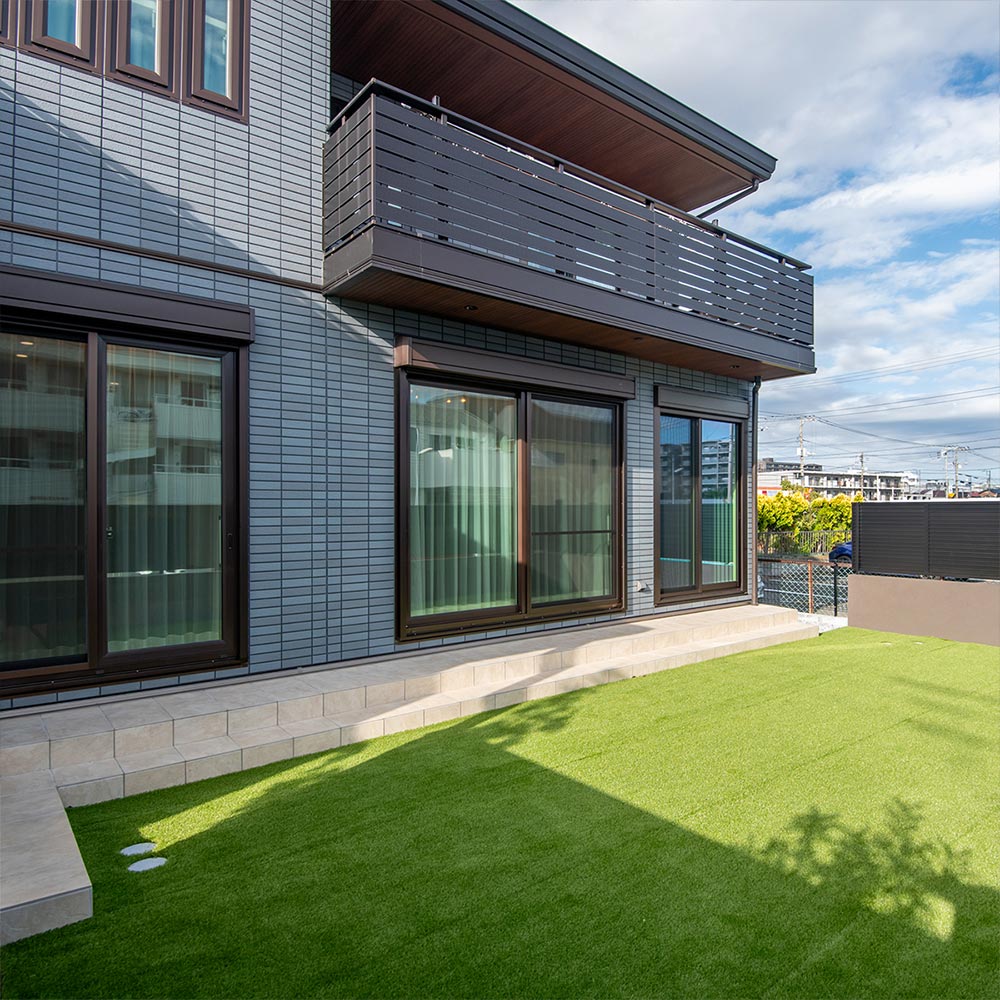 イメージ_東京セキスイハイム建築事例_緑の芝生が広がる庭に、温かみのあるアイボリーのタイルテラスを設置